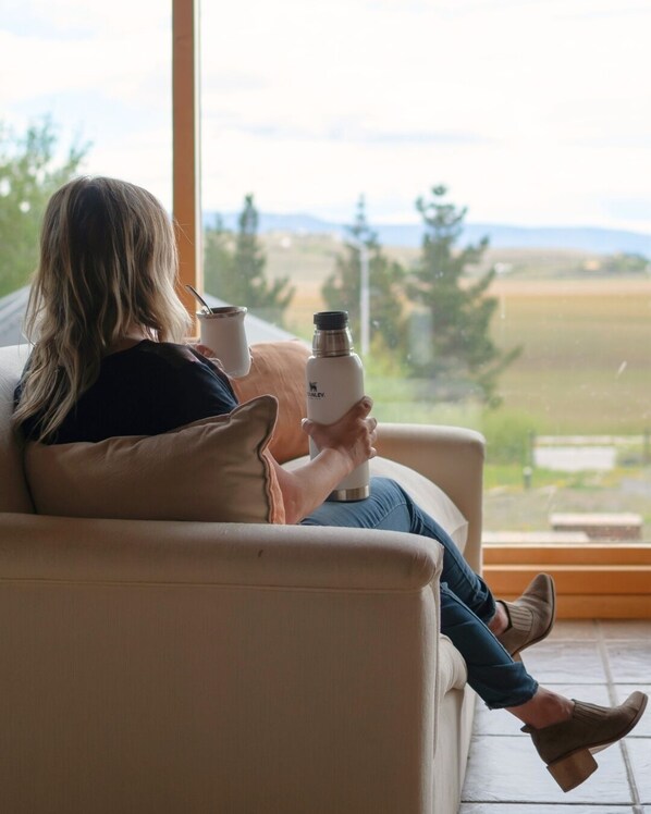 A person sitting on a couch with a view of a landscape through a window.