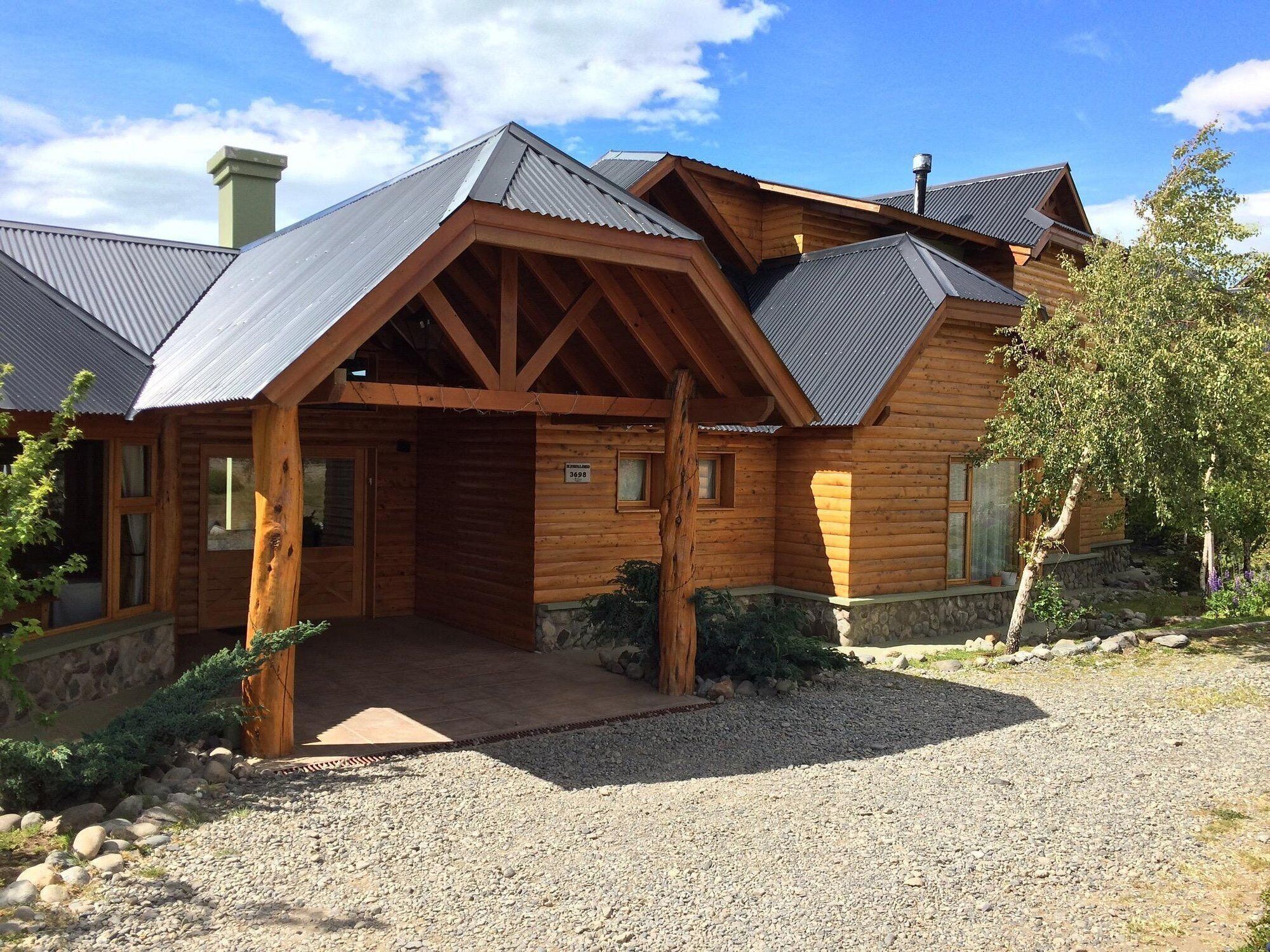 A wooden cabin with a gravel driveway and a stone wall.