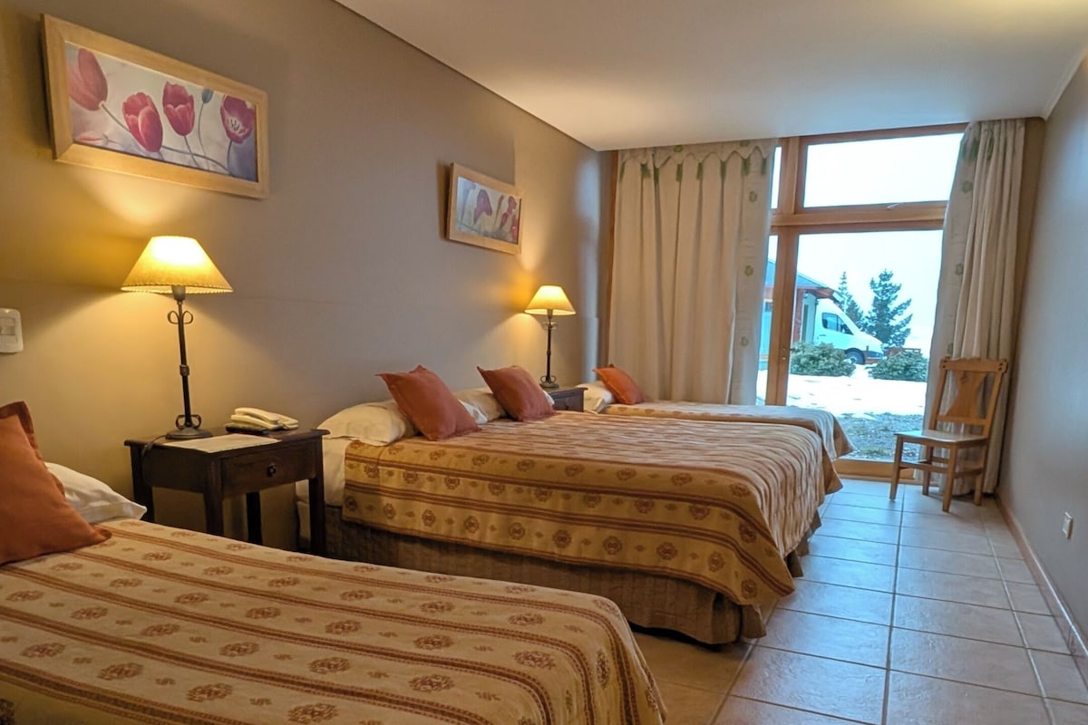 A hotel room with two beds, a window with curtains, a lamp, and a painting on the wall.