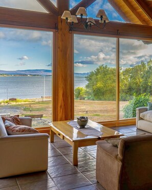 Una habitación amplia con ventanas grandes que ofrecen vistas a un lago y montañas lejanas.