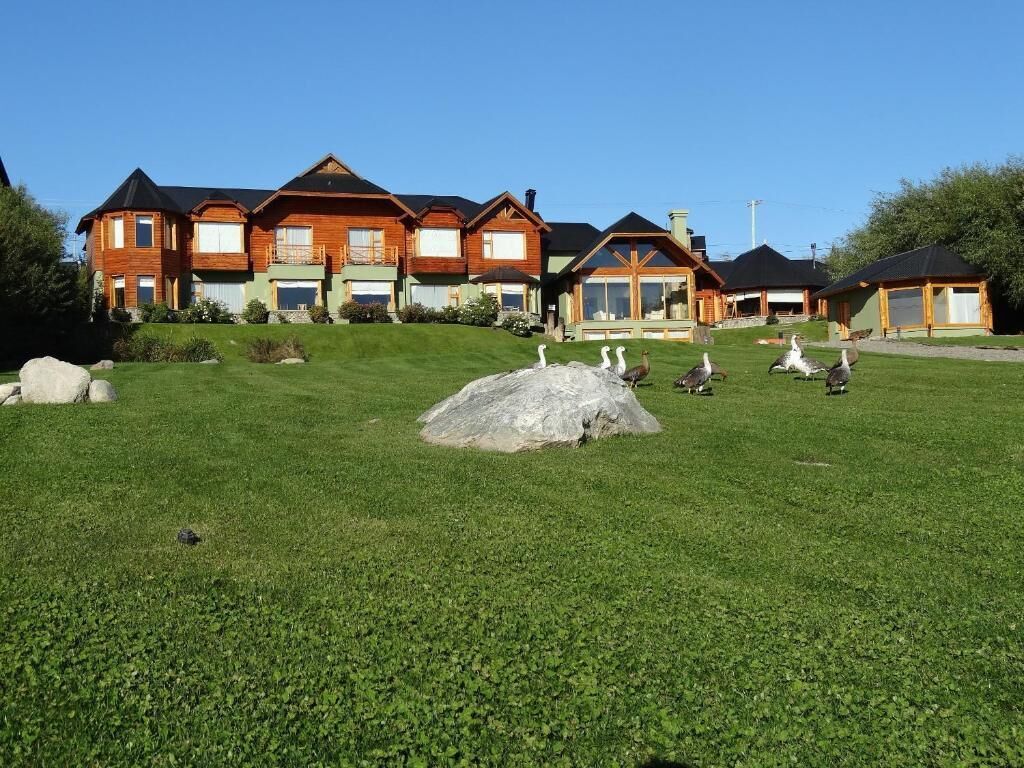 Une grande maison en bois à plusieurs étages, dotée d’une pelouse bien entretenue et d’un grand rocher décoratif en premier plan.