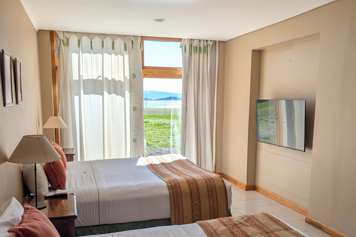 Quarto de hotel com duas camas, televisão e janela com vista para o exterior.