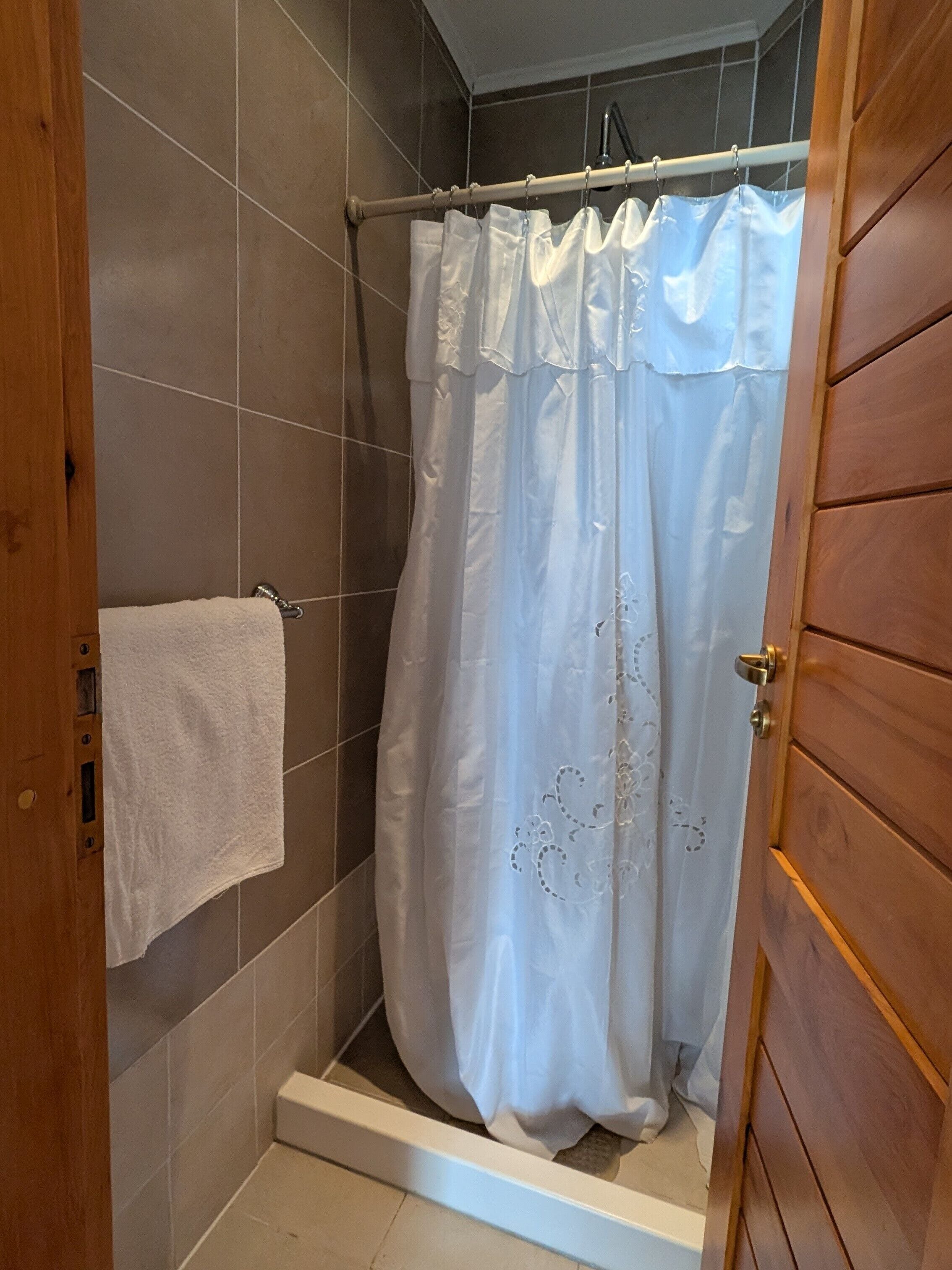 A shower with a white curtain, a white towel hanging on the wall, and a wooden door.