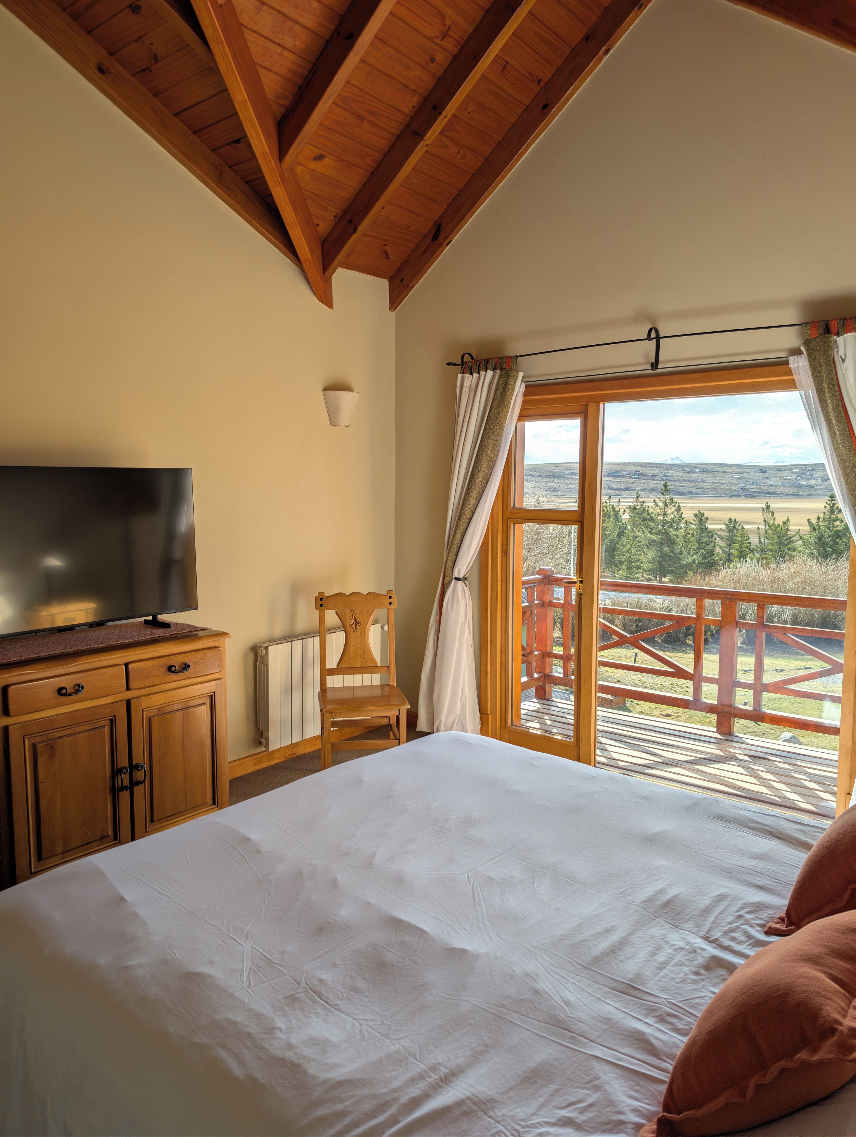 Un dormitorio con cama, cómoda de madera, televisión y vistas a una terraza y paisaje.