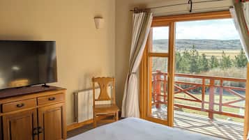 Un dormitorio con cama, cómoda de madera, televisión y vistas a una terraza y paisaje.