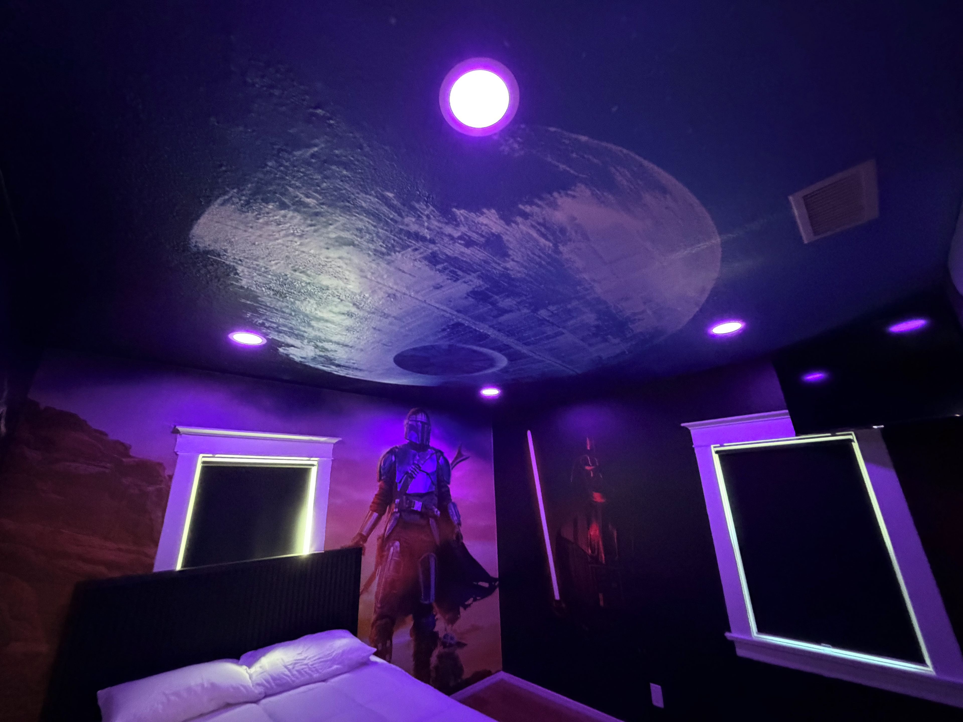 Une pièce comprenant un lit, une peinture murale au plafond et deux lampes fixées au mur.