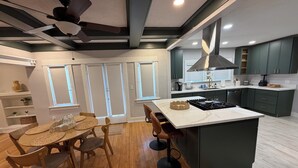 Une cuisine moderne avec un îlot central, des meubles de couleur sombre et un ventilateur de plafond.