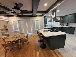 Une cuisine moderne avec un îlot central, des meubles de couleur sombre et un ventilateur de plafond.