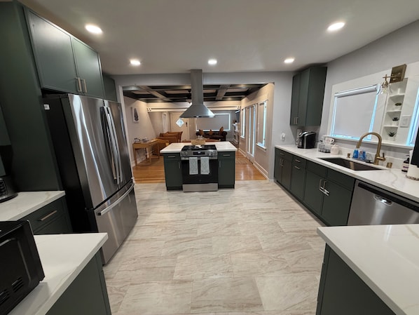 A modern kitchen with a central island, stainless steel appliances, and a view into the living area.