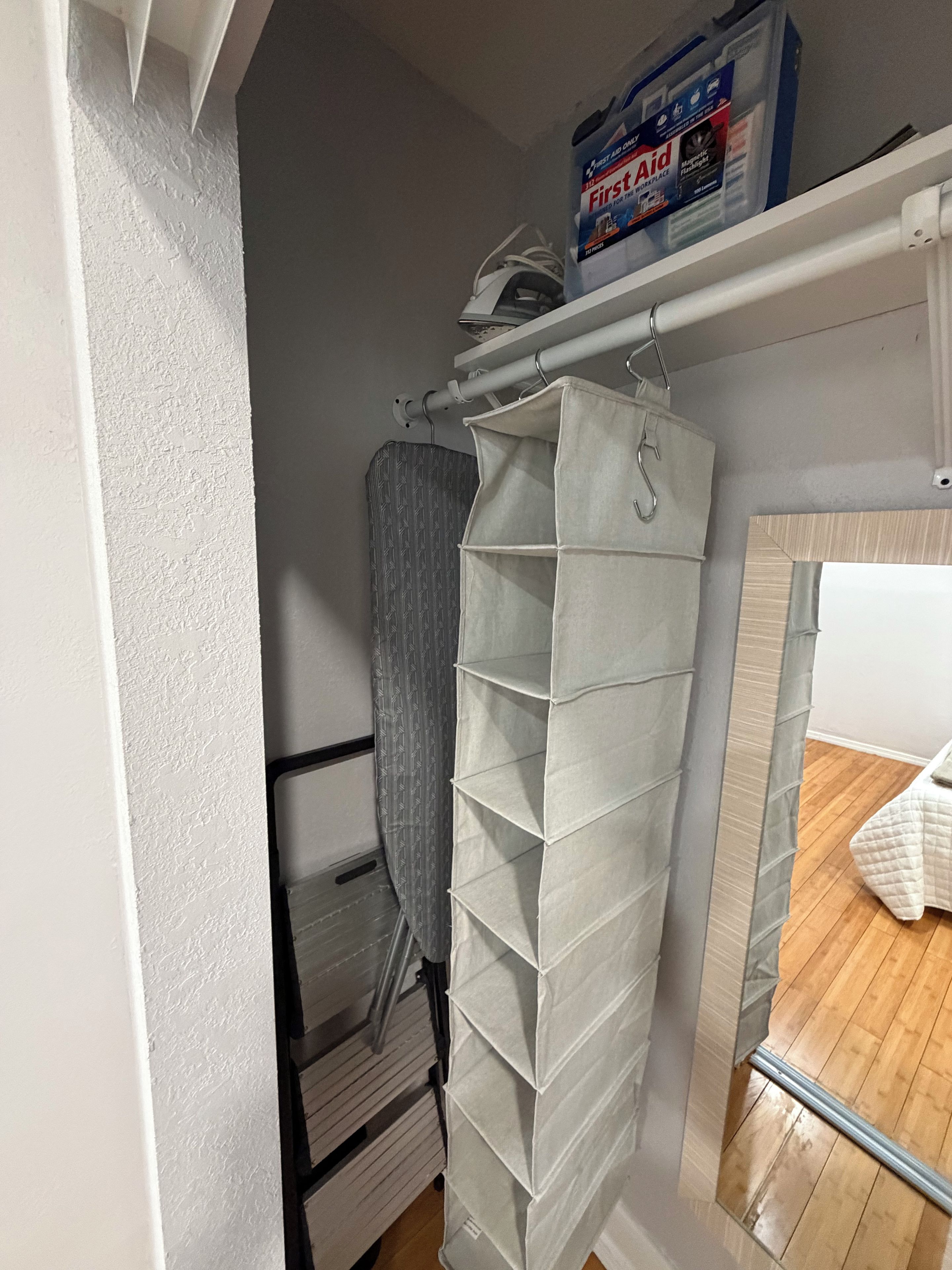 Un meuble de rangement doté de plusieurs compartiments, un rideau de douche et une boîte étiquetée « Trousse de premiers secours » posée sur une étagère.