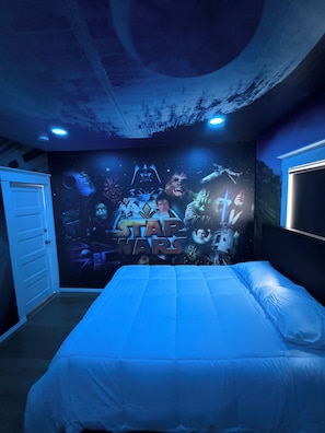 Une chambre avec une fresque murale sur le thème de Star Wars, un lit avec une literie blanche et une porte sur le côté gauche.