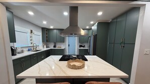 Une cuisine moderne dotée d’un îlot central, de meubles de couleur sombre et d’une hotte de cuisson en acier inoxydable.