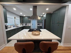 Une cuisine moderne dotée d’un îlot central, de meubles de couleur sombre et d’une hotte de cuisson en acier inoxydable.