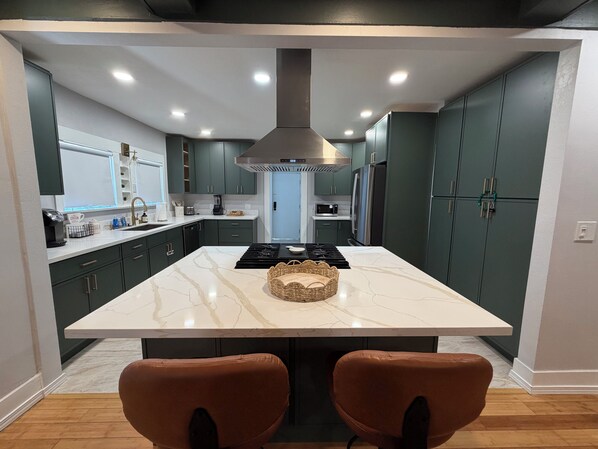 Une cuisine moderne dotée d’un îlot central, de meubles de couleur sombre et d’une hotte de cuisson en acier inoxydable.