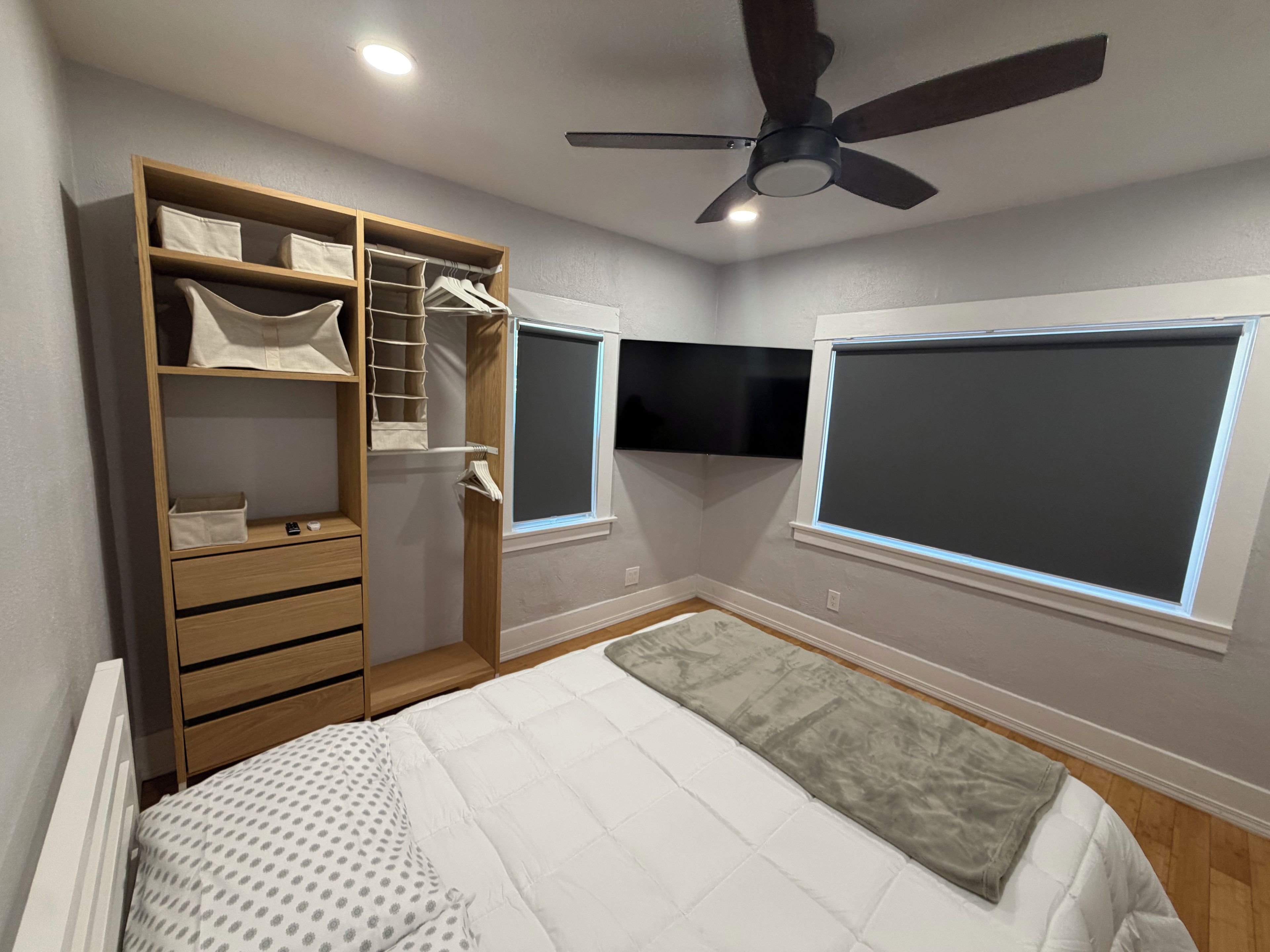 Une chambre à coucher comprenant un lit, une armoire, un ventilateur de plafond et deux fenêtres.