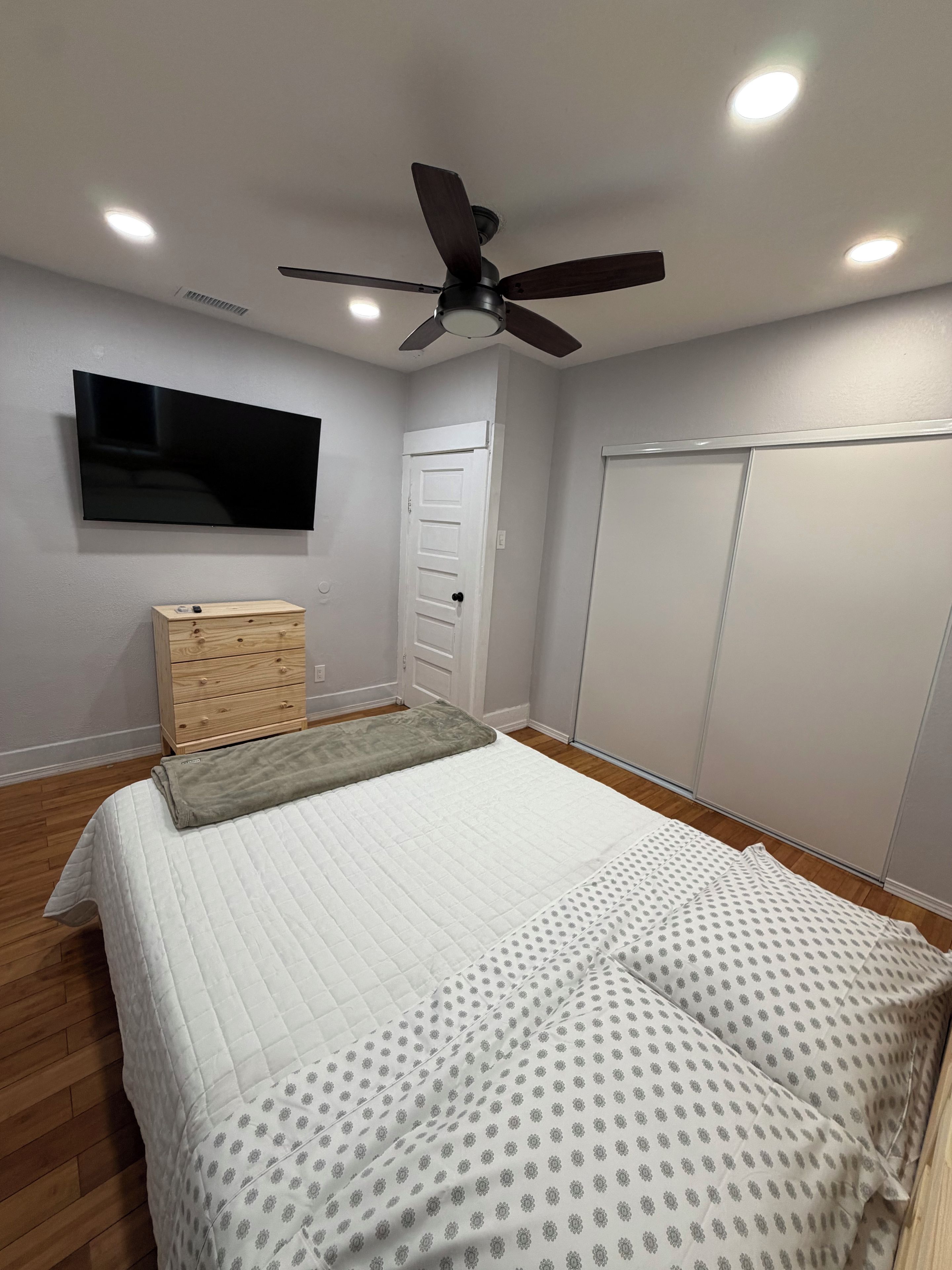 A bedroom with a bed, a television, a ceiling fan, and a wardrobe.