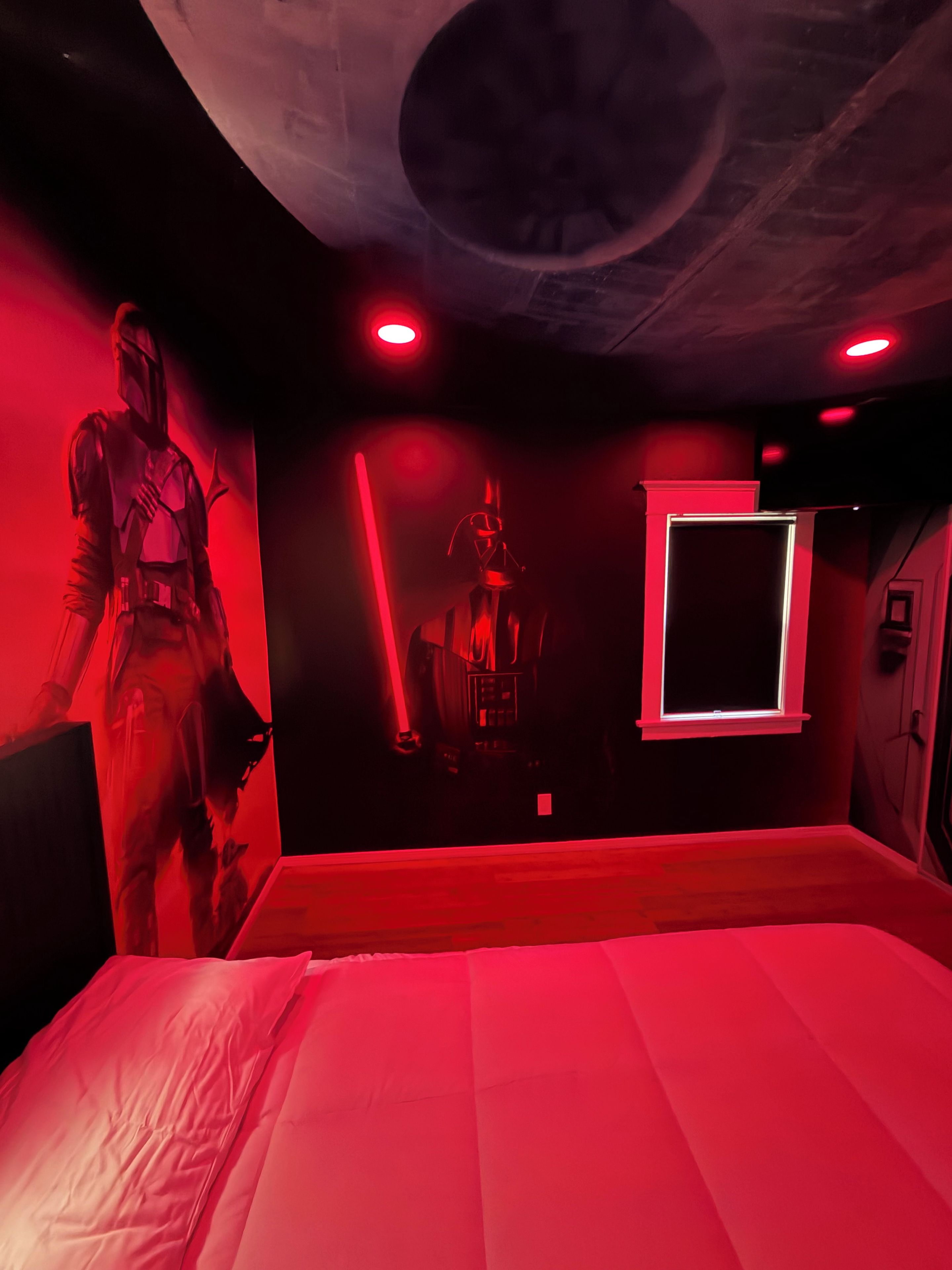 A room with a bed, a wall-mounted TV, and two figures resembling characters from a science fiction series.