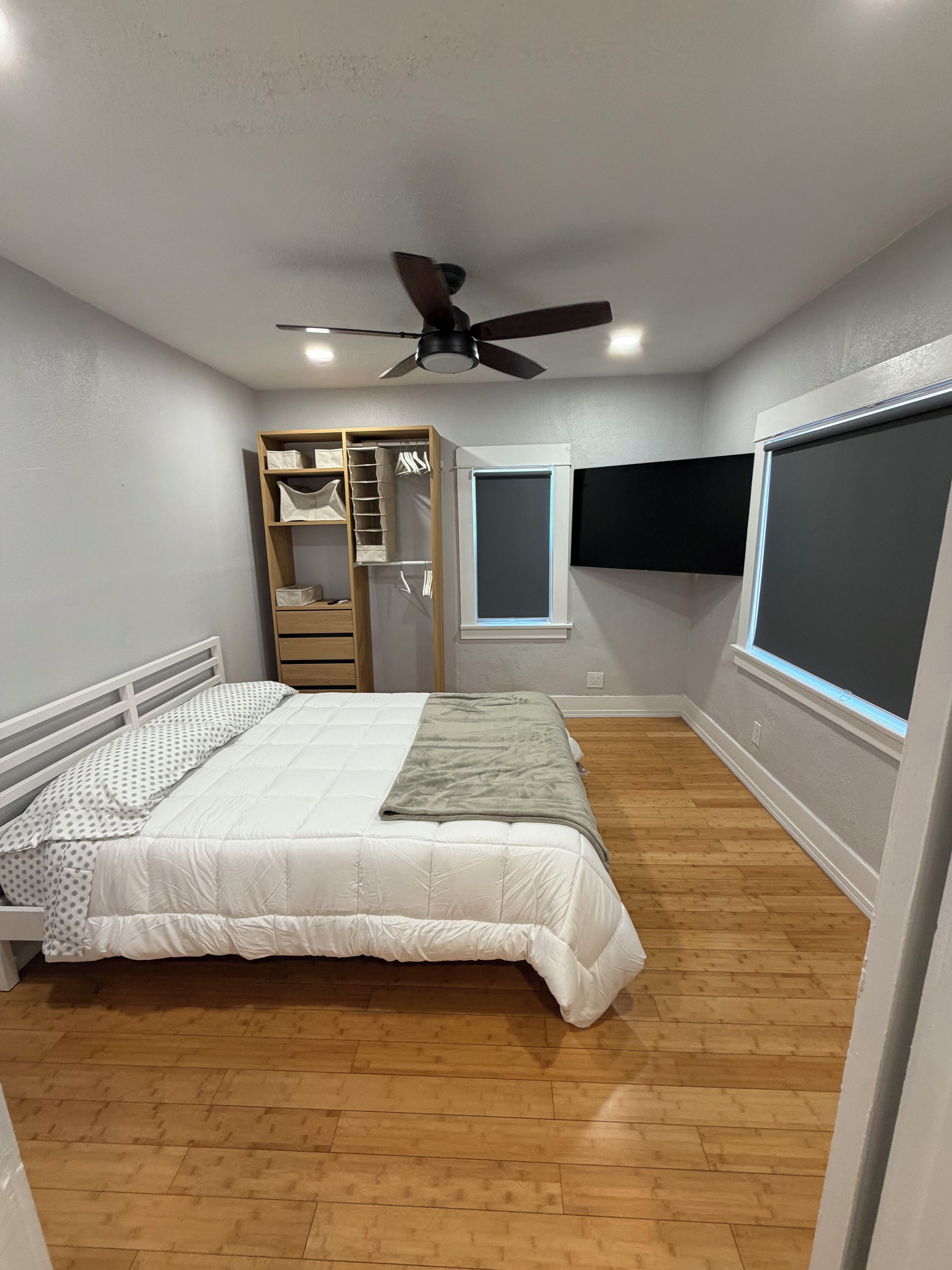 Une chambre à coucher avec un lit, une armoire en bois, un ventilateur de plafond et une fenêtre.