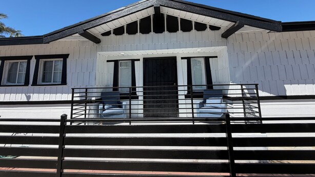 Un bâtiment à l’extérieur blanc, avec un toit noir et une entrée fermée par un portail.