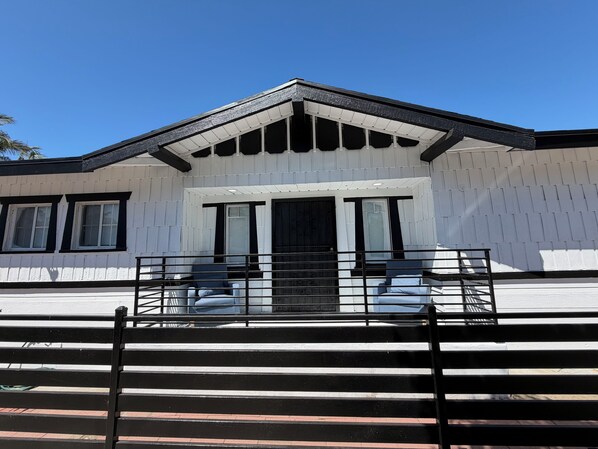Un bâtiment à l’extérieur blanc, avec un toit noir et une entrée fermée par un portail.