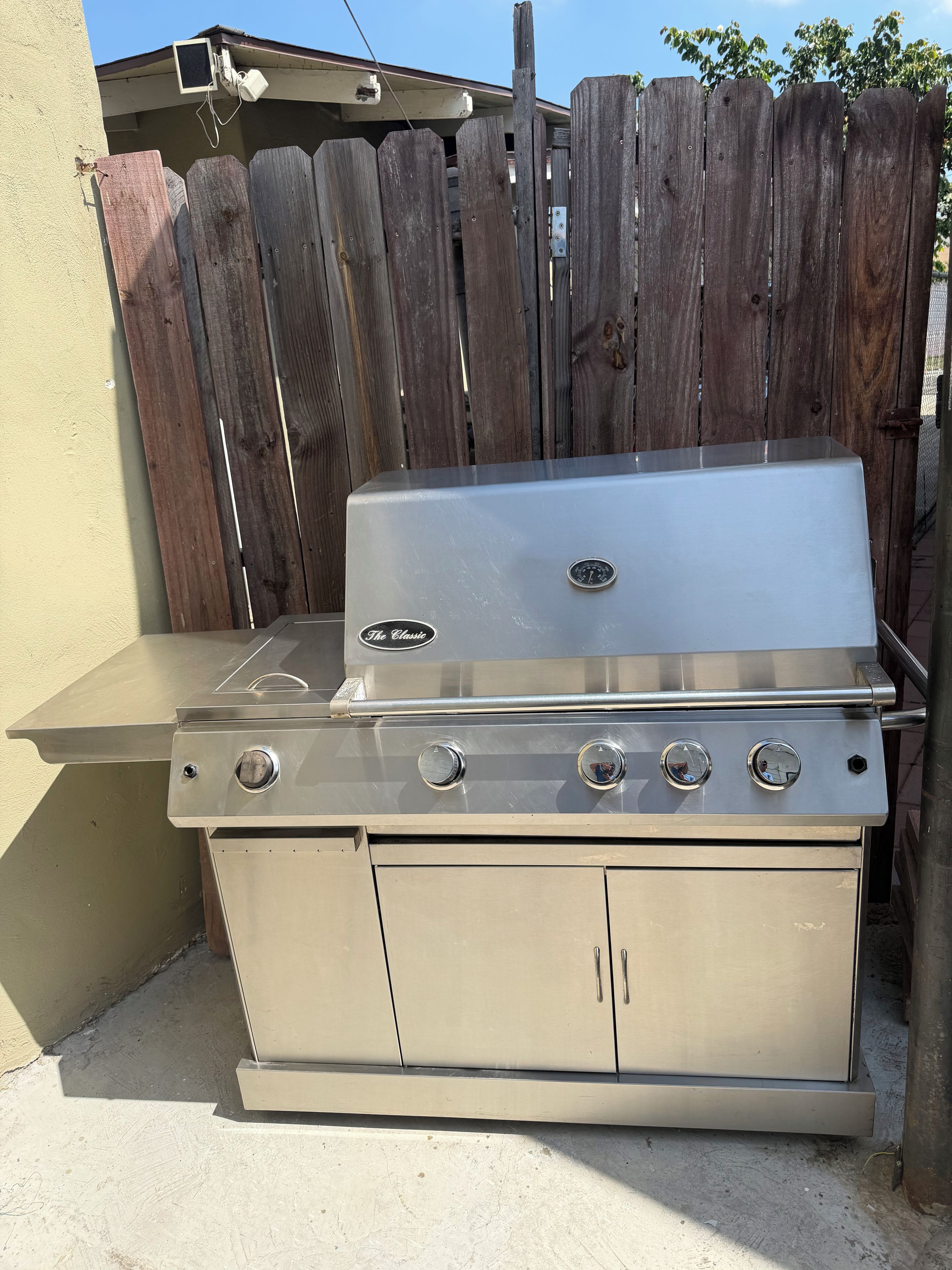Un barbecue extérieur en acier inoxydable doté de quatre brûleurs, d’un évier intégré et d’un meuble de rangement.