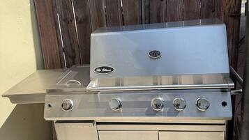 A stainless steel outdoor grill with four burners, a built-in sink, and a storage cabinet.