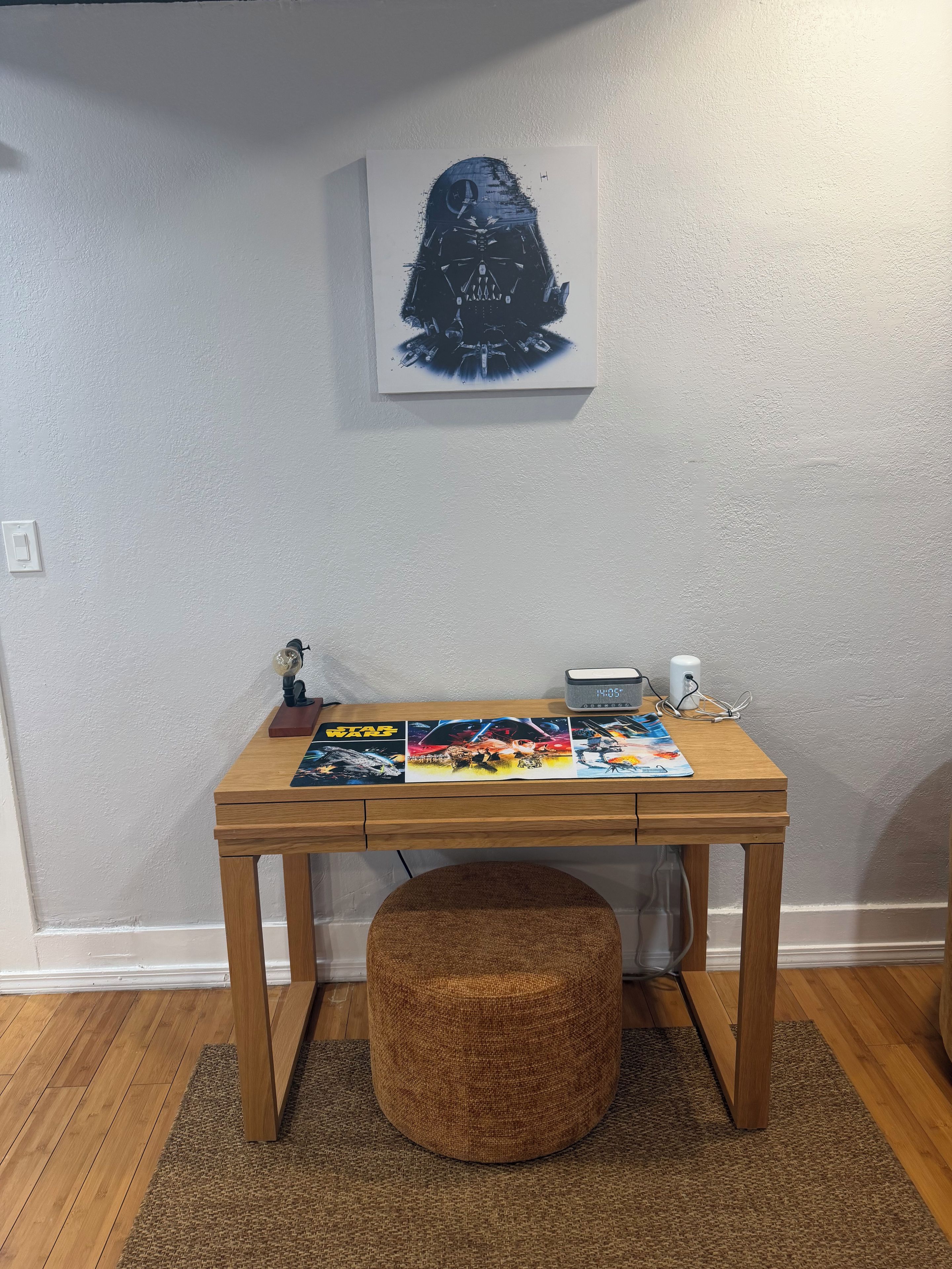 Un escritorio de madera con un cartel de temática Star Wars, un reloj y una figurita.