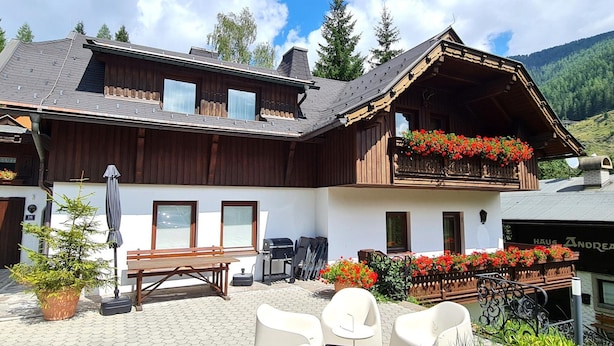 En byggnad i chaletstil med en balkong, utomhusmöbler och en bergskuliss i bakgrunden.