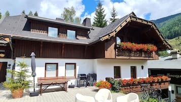 A chalet-style building with a balcony, outdoor seating, and a mountain backdrop.