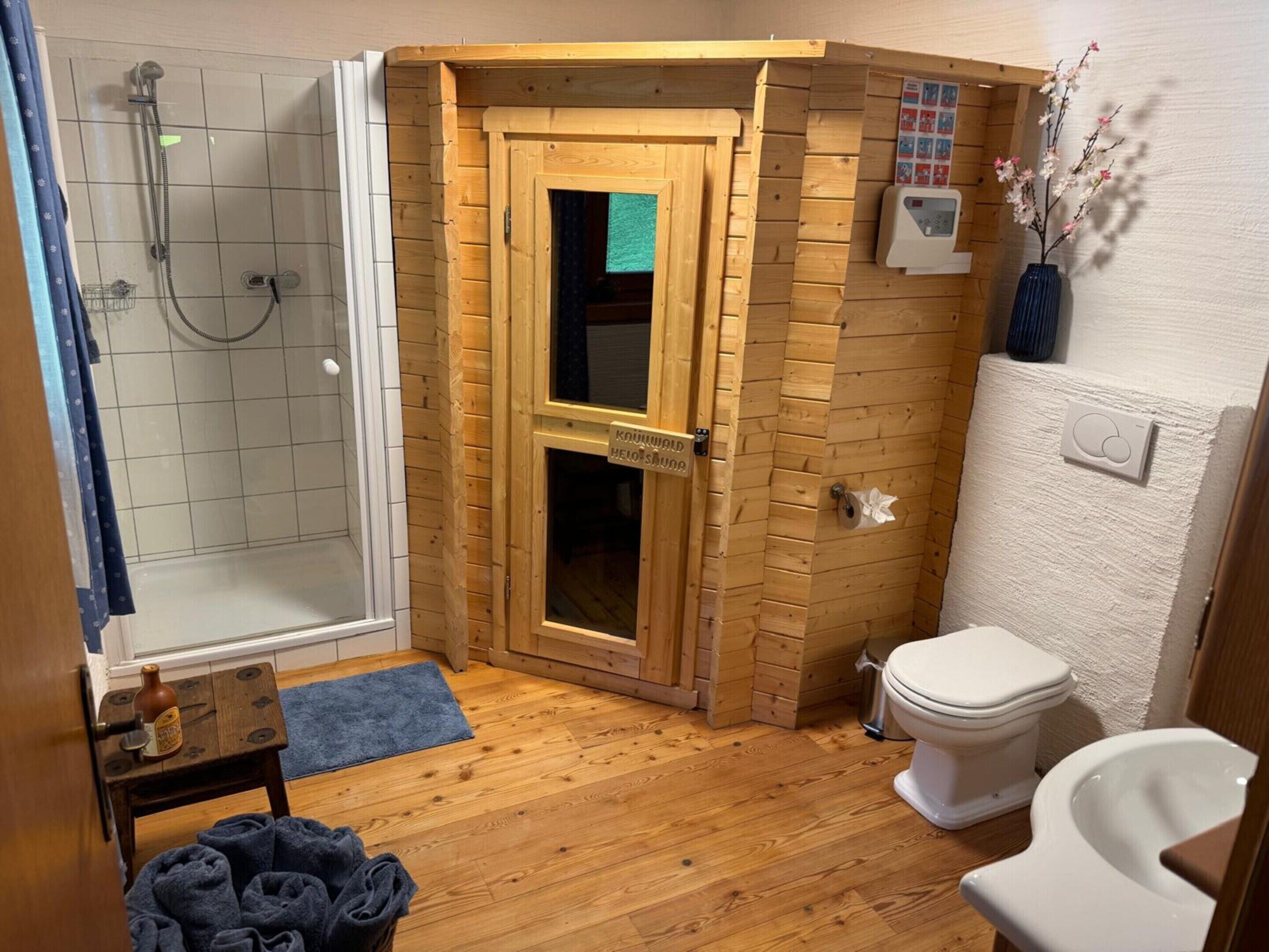 A small, compact bathroom with a shower, toilet, and a wooden door leading to a storage area.
