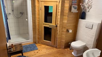 A small, compact bathroom with a shower, toilet, and a wooden door leading to a storage area.