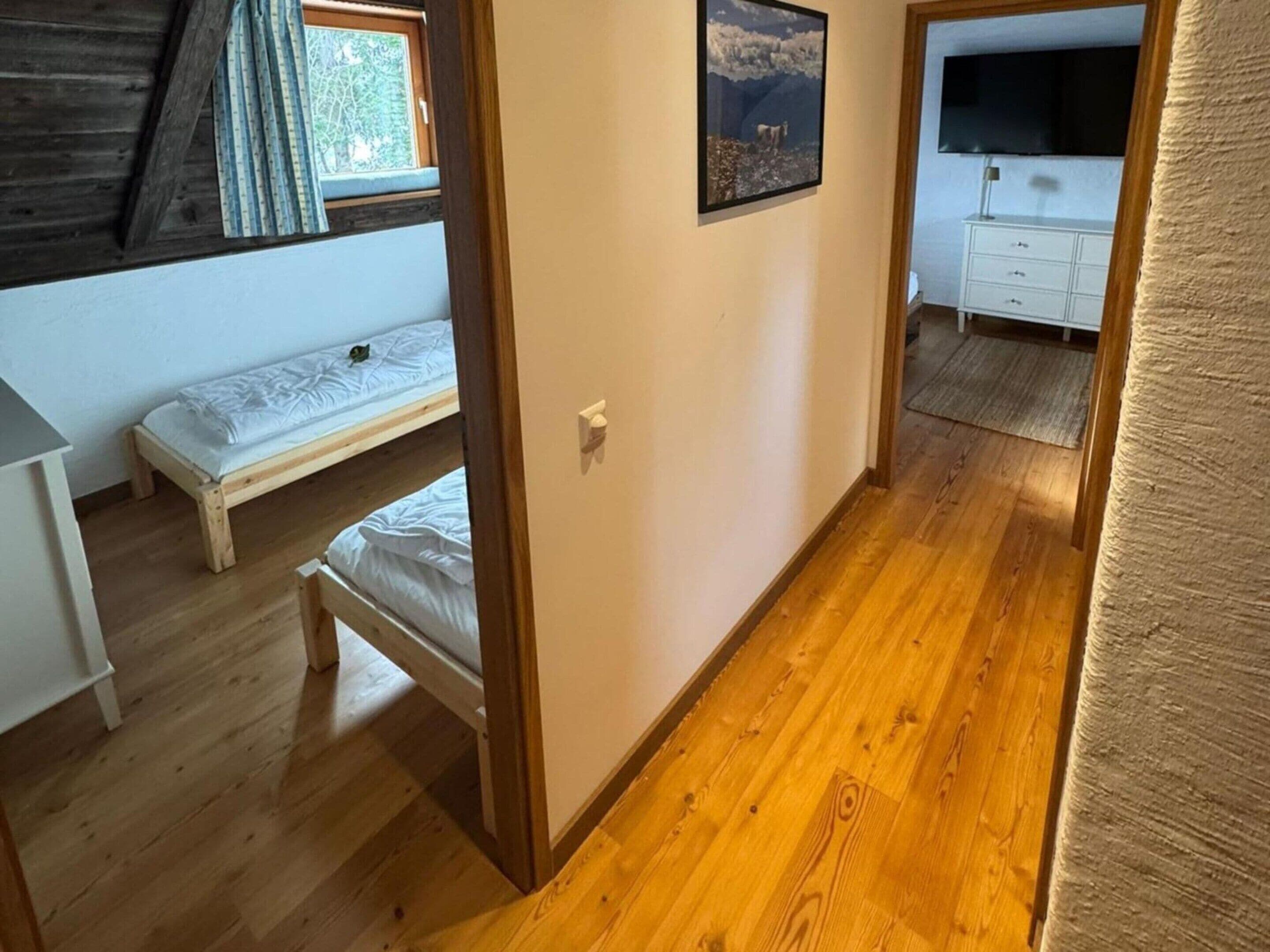 A room with a wooden floor, a bed, a window with curtains, a picture on the wall, and a white dresser.