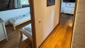 A room with a wooden floor, a bed, a window with curtains, a picture on the wall, and a white dresser.