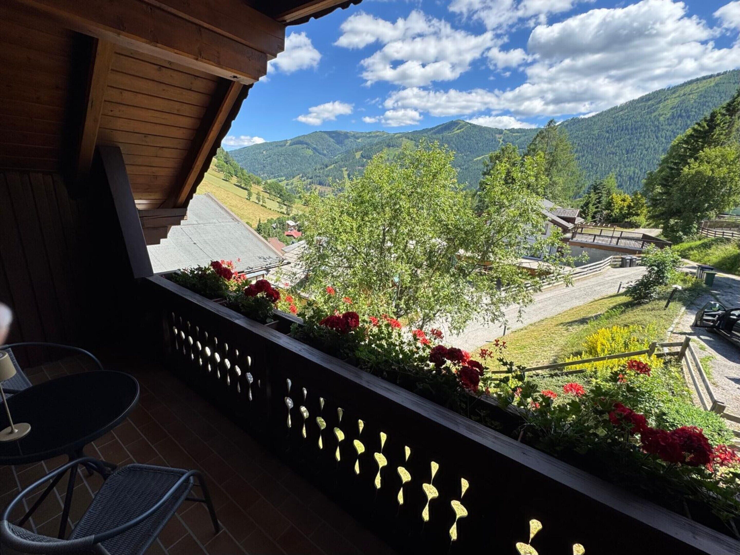 A balcony with a view of a mountainous landscape, a wooden ceiling, and a chair.