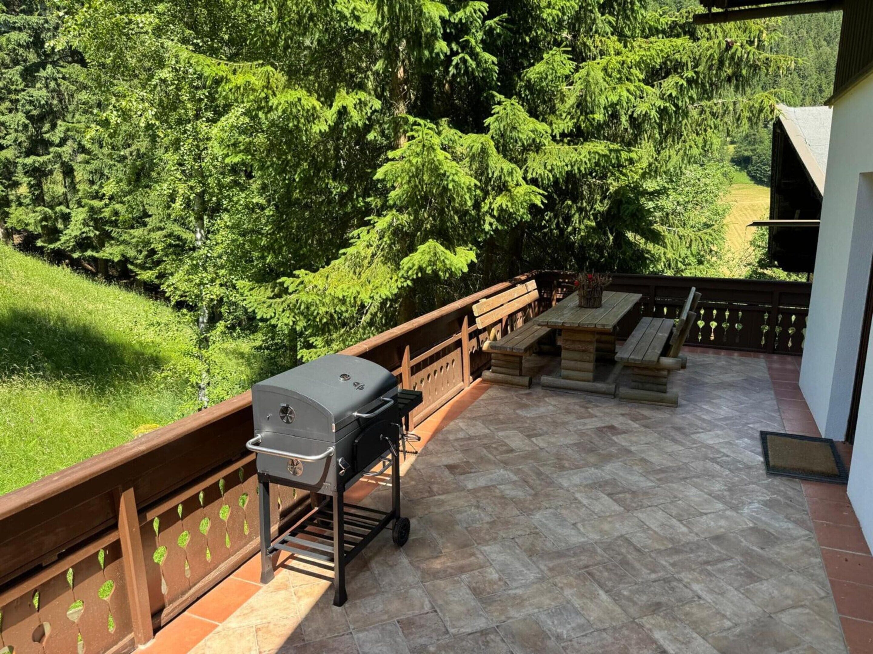 A patio with a grill, outdoor seating, and a view of a forested area.
