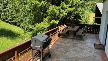 A patio with a grill, outdoor seating, and a view of a forested area.