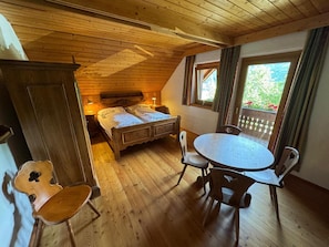 A room with a wooden ceiling, a bed with a headboard, a round table with chairs, and a window with curtains. - Landhaus Finkenhof (Bad Kleinkirchheim)