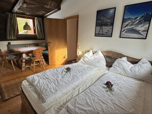 Een slaapkamer met een houten bed, een bureau en stoelen, een raam met gordijnen en twee ingelijste foto's aan de muur.