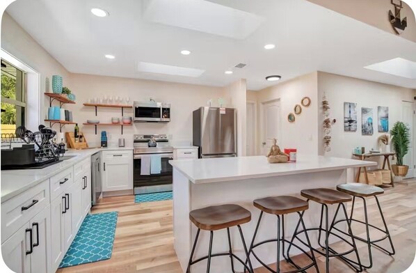 A modern kitchen with white cabinetry, a central island with stools, and a microwave above the counter.