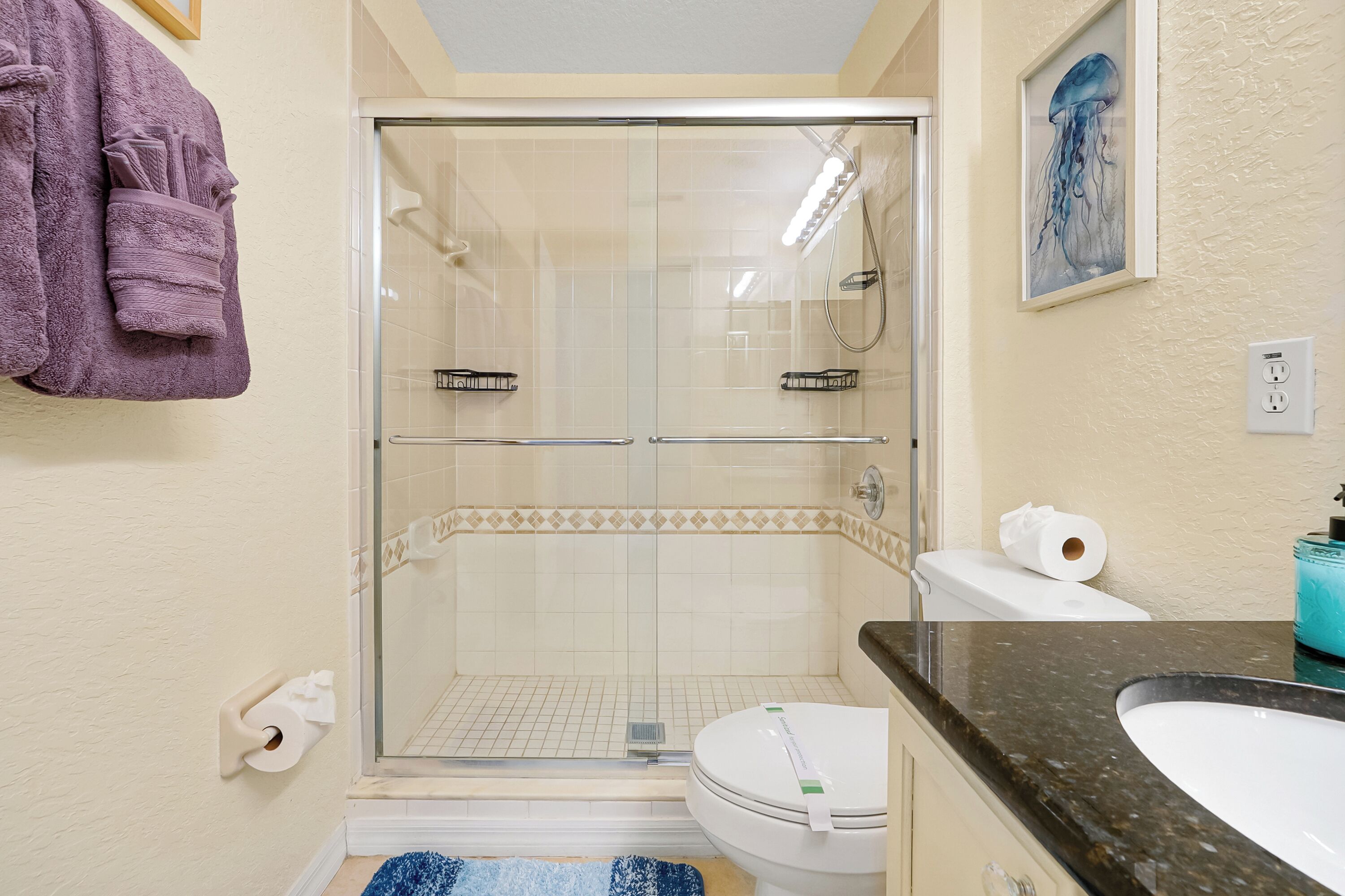 A bathroom with a glass-enclosed shower, a toilet, a sink, and a towel rack with towels.