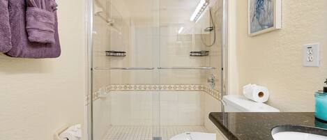 A bathroom with a glass-enclosed shower, a toilet, a sink, and a towel rack with towels.