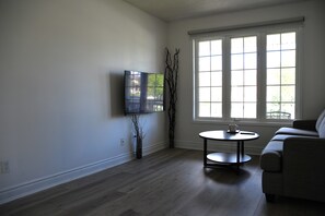 A living room with a flat-screen TV mounted on the wall, a round table with a remote control, and a sofa.