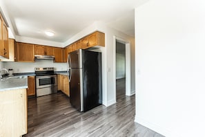 A modern kitchen with wooden cabinets, stainless steel appliances, and a dark wood floor. - Cozy 3BR Barrie Home Near Snow Valley Lake & Downtown (Barrie)