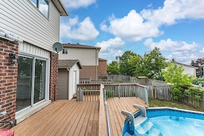 A backyard with a wooden deck, a swimming pool, and a brick wall.