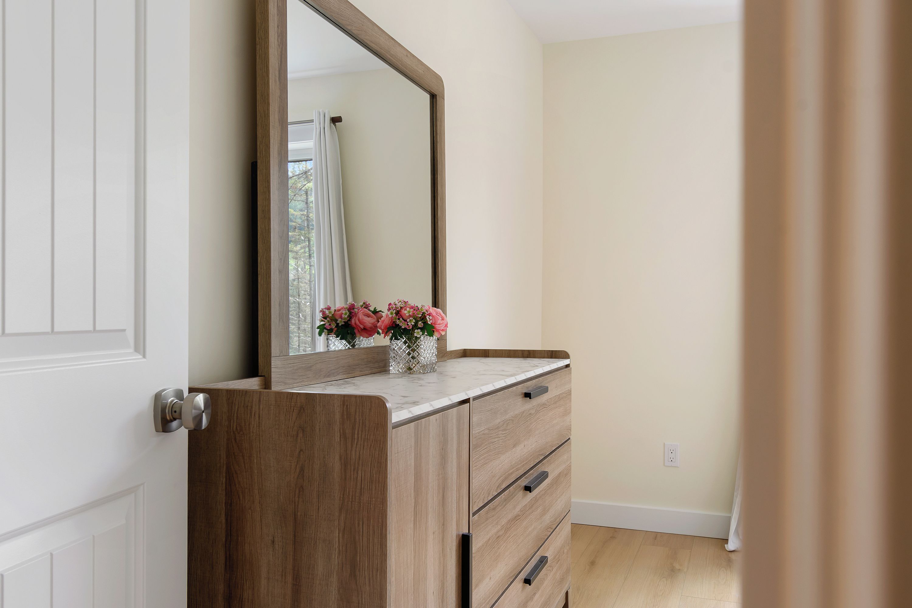 Un baño con tocador de madera, espejo y un florero con flores.
