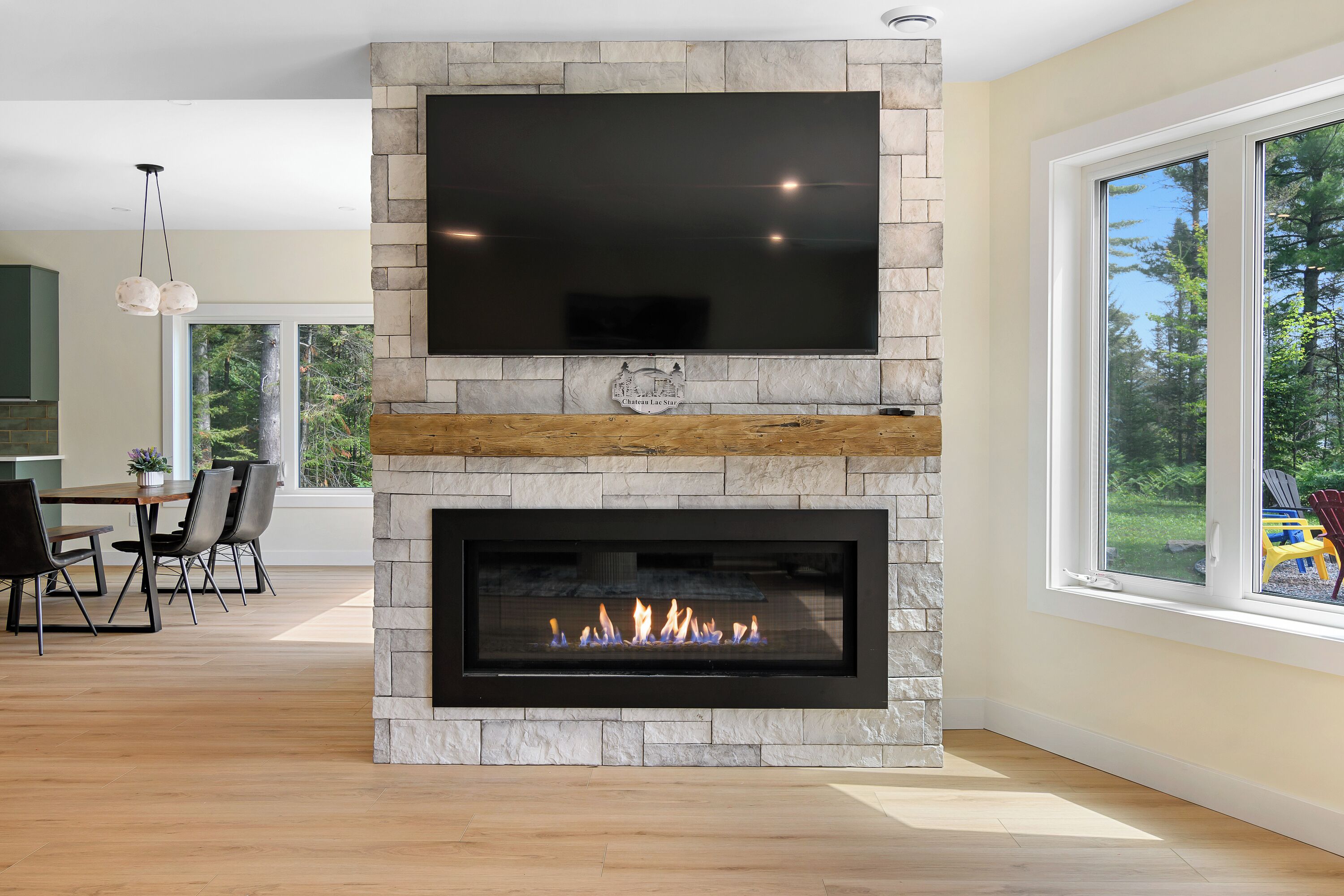 Una sala de estar moderna con chimenea de piedra, un televisor de pantalla plana montado encima y un comedor con sillas y una mesa.