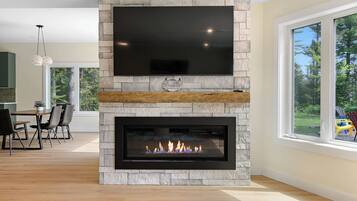 Una sala de estar moderna con chimenea de piedra, un televisor de pantalla plana montado encima y un comedor con sillas y una mesa.
