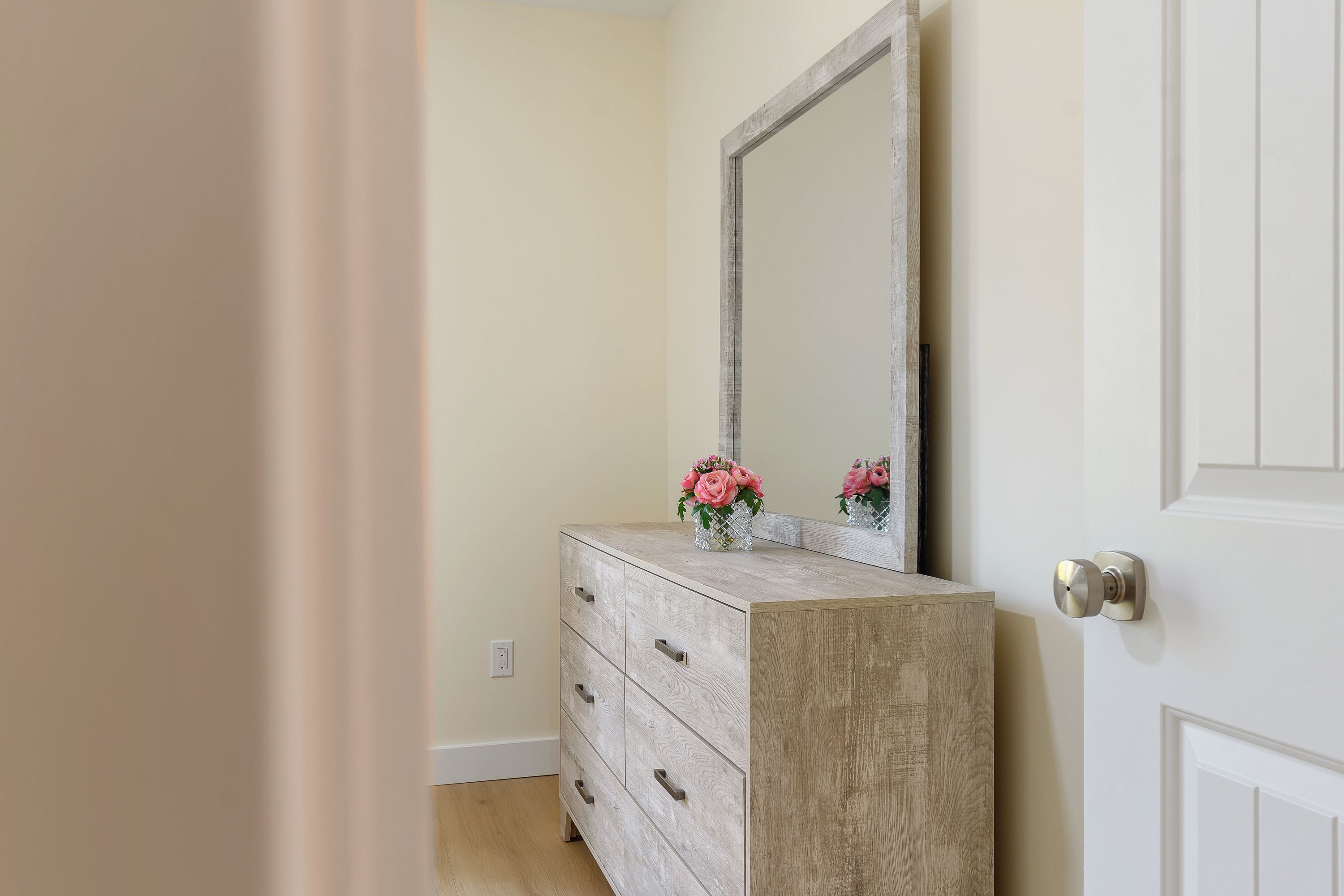 A room with a wooden dresser, a mirror, and a door with a round handle.