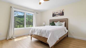 Un dormitorio con cama, ventilador de techo, ventana con cortinas y un cuadro en la pared.
