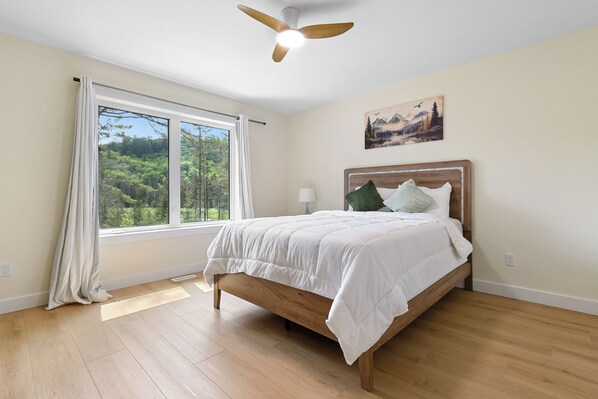 A bedroom with a bed, a ceiling fan, a window with curtains, and a painting on the wall.